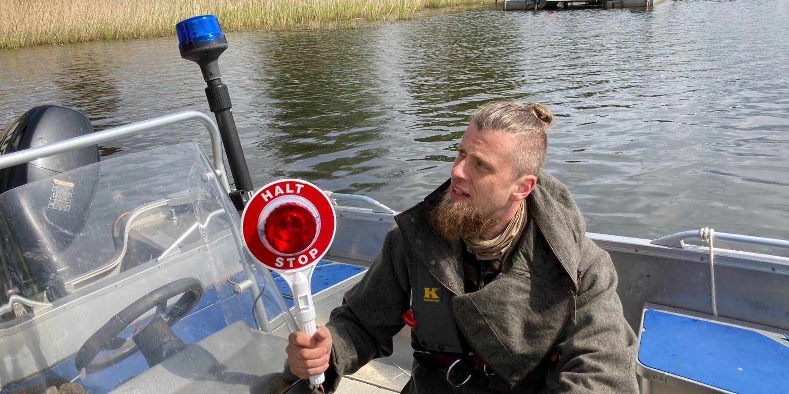 Ein Mann hockt mit einer "Halt! Stop!"-Winkekelle in einem Boot