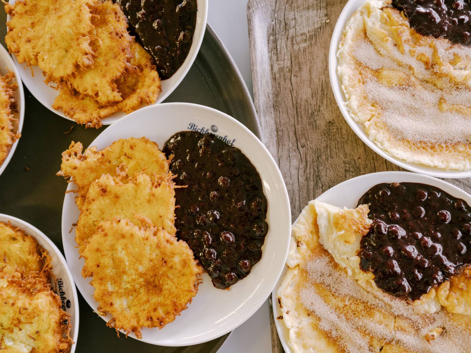 Auf mehreren Tellern sind Kartoffelpuffer, Eierpfannkuchen und jeweils daneben Blaubeerkompott mit ganzen Blaubeeren.