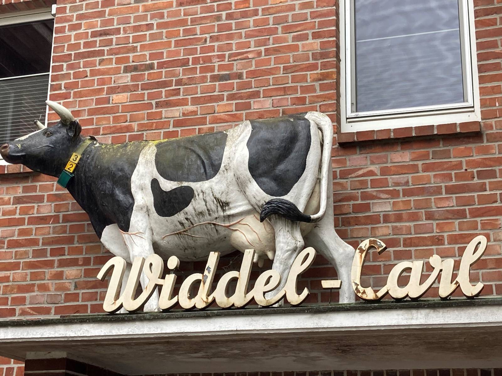 Eingang eines Bauernhofes mit dem Schriftzug Widdel-Carl und einer lebensgroßen Kuhfigur