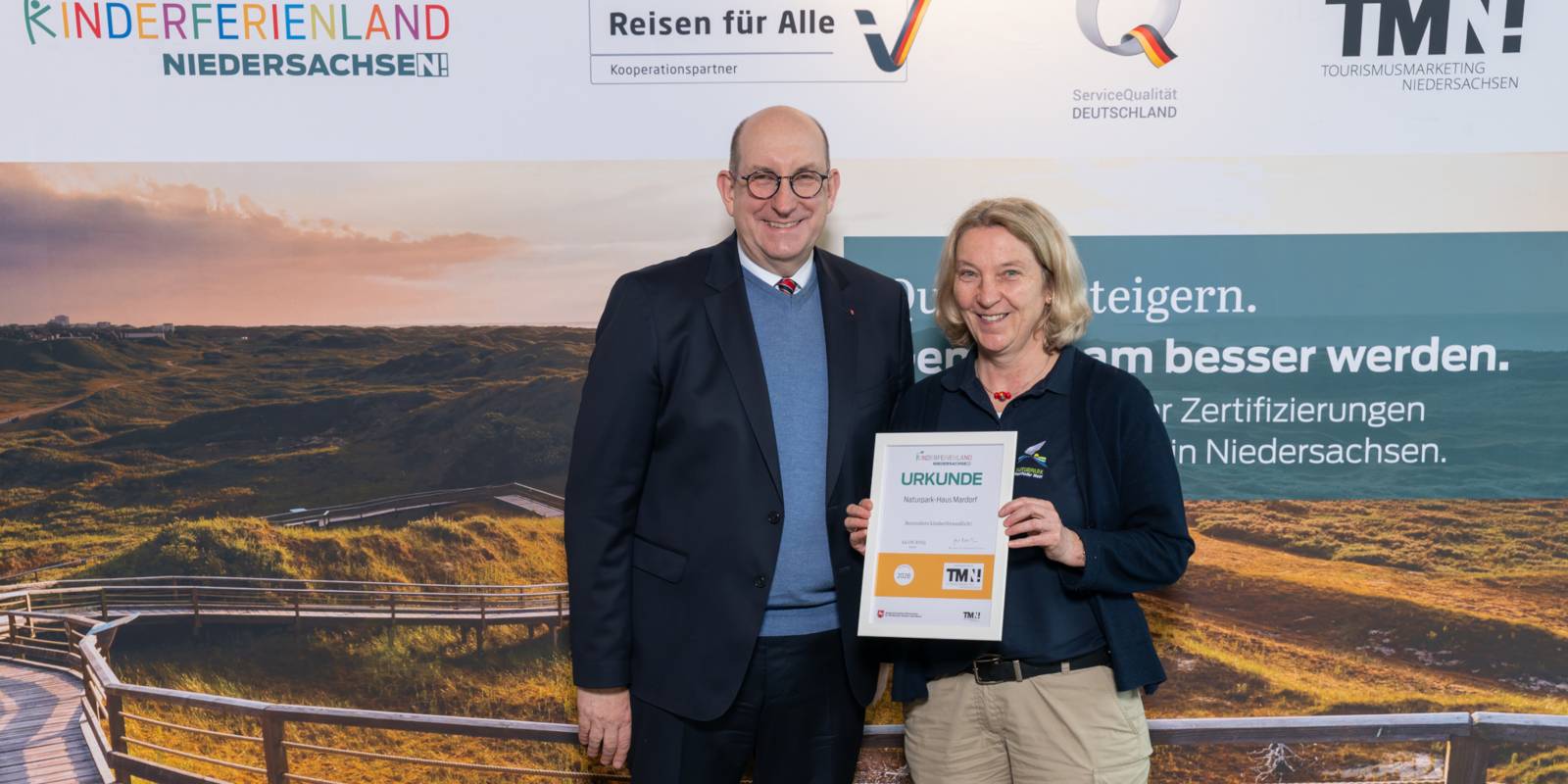 Zwei Personen stehen nebeneinander, eine hält eine Urkunde in den Händen.