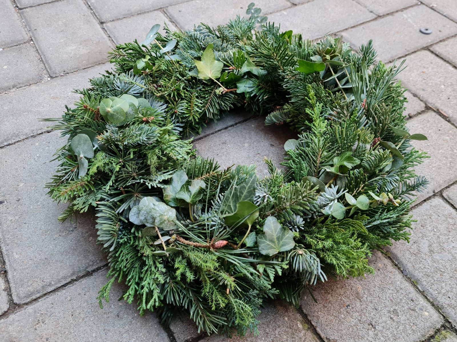Ein Adventskranz liegt auf einer gepflasterten Fläche.
