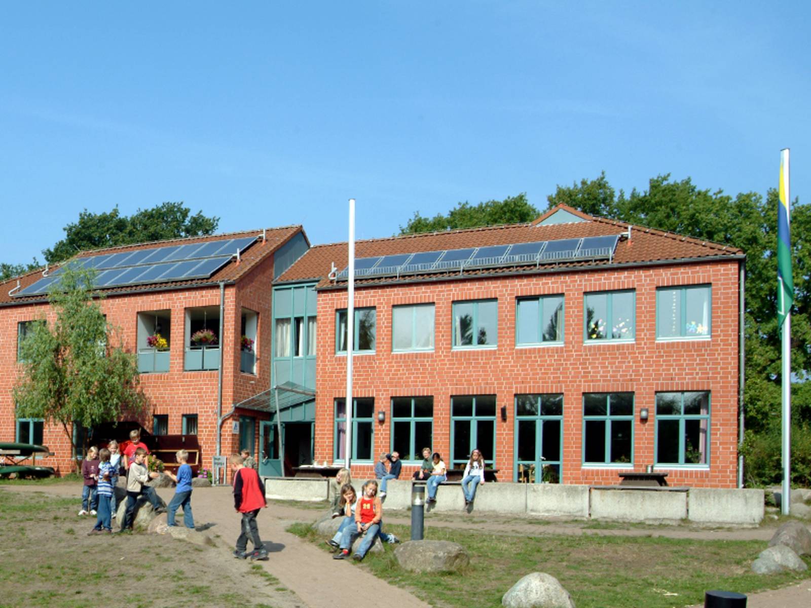 Kinder spielen vor einem Zweigeschossigen Gebäude aus roten Backsteinen.