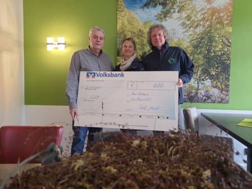 Drei Personen bei der Übergabe eines überdimensional großen Schecks.