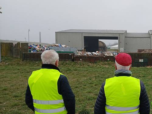 Personen tragen leuchtende Warnkleidung und Blicken im Rahmen einer Führung auf ein Entsorgungszentrum