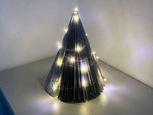 Gefaltete Seiten einer Zeitschrift bilden einen freistehenden Weihnachtsbaum, dekoriert mit einer Lichterkette.