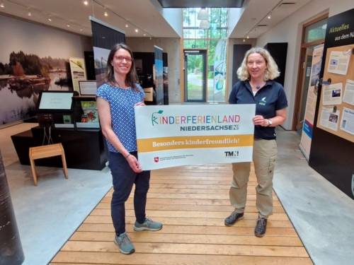 Zwei Personen halten ein Plakat: Kinderferienland Niedersachsen - Besonders Kinderfreundlich