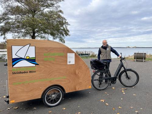 Mann mit einem Gespann aus E-Bike und Fahrrad-Wohn-Anhänger