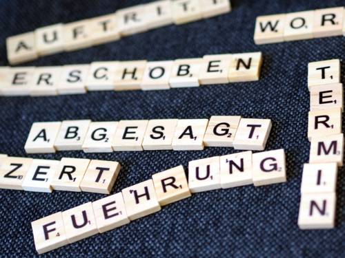 Spielsteine liegen auf einem Untergrund aus Stoff, sie bilden die Worte "Abgesagt" und "Termin".