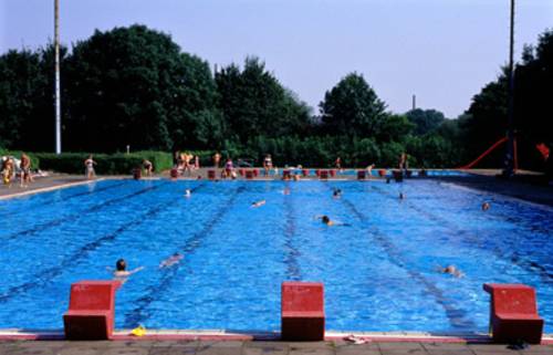 Blick auf das Schwimmerbecken, einige Schwimmer sind im Wasser, im Hintergrund stehen ein paar Menschen am Beckenrand