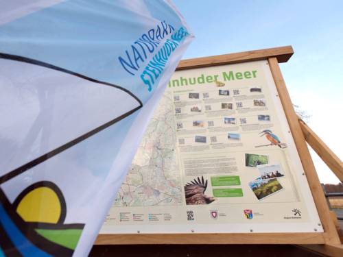 Eine Strandfahne mit Naturparklogo steht vor einer Naturpark-Infotafel.