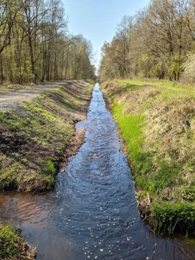 Blick von oben auf einen geraden Entwässerungsgraben bis zum Horizont. Der Entwässerungsgraben ist mit etwas Wasser gefüllt.