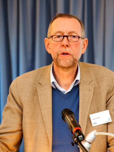Ein Mann steht hinter einem Mikrofon und vor einem blauen Vorhang.