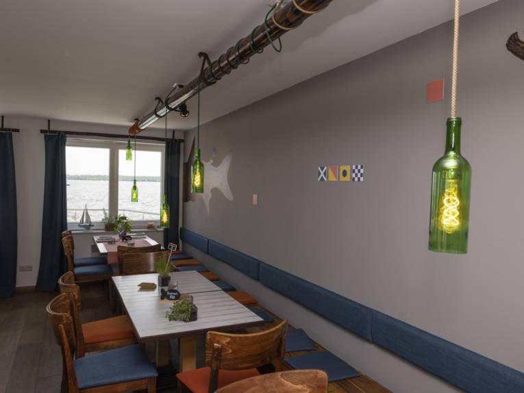 Der Innenraum des Restaurants mit Holzstühlen, blauen Sitzkissen, grünen Lampen