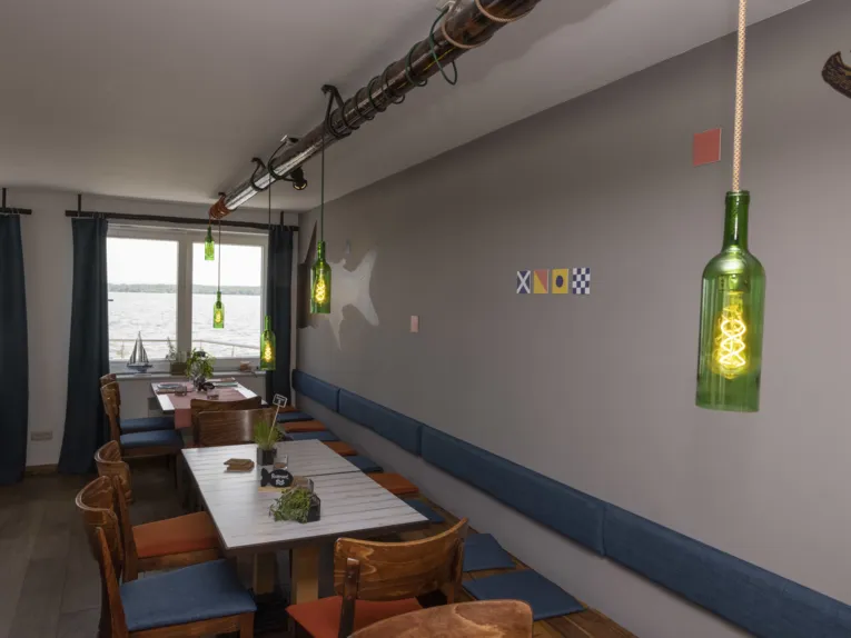 Der Innenraum des Restaurants mit Holzst&uuml;hlen, blauen Sitzkissen, gr&uuml;nen Lampen