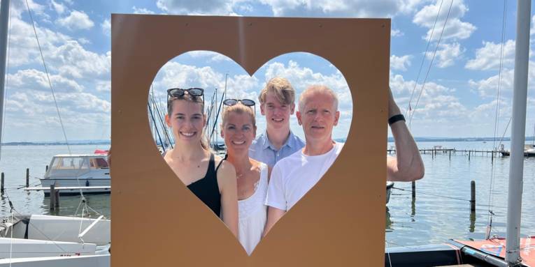 Personen stehen mit an einem Steg und schauen durch eine Herz-Schablone