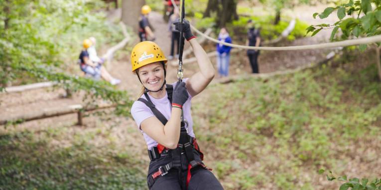 Eine Person hängt an einem Seil, im Hintergrund sind weiterer Personen und Klettermöglichkeiten