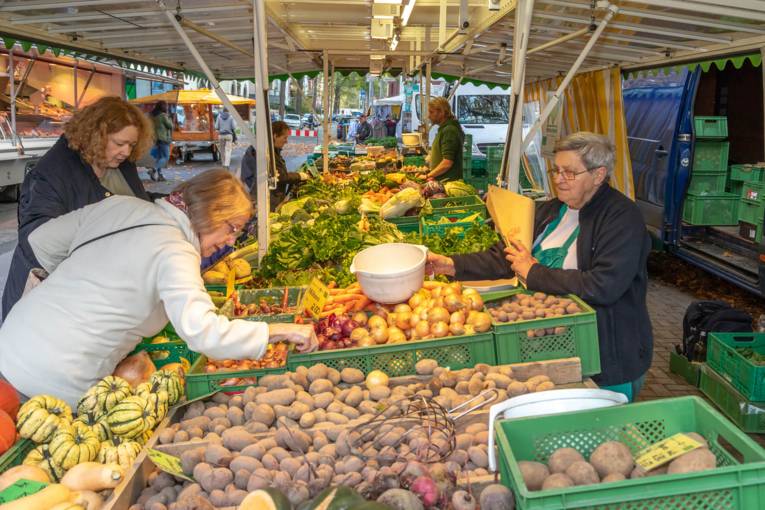 Kundinnen begutachten die Waren an einem Gemüsetand auf dem Wochenmarkt.