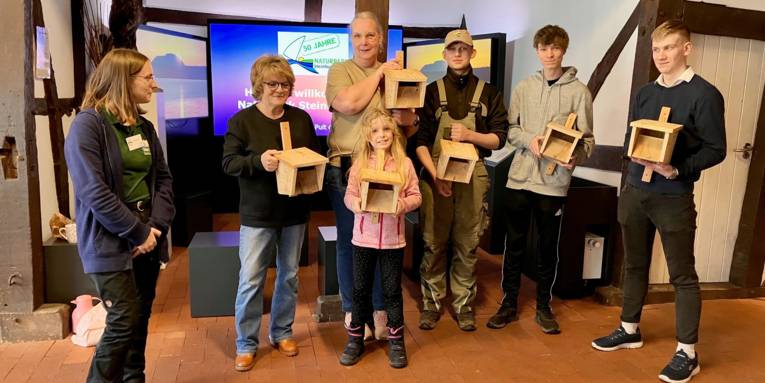 Sieben stehen in der Infoscheune Naturpark Steinhuder Meer und halten Vogelhäuschen in die Kamera.