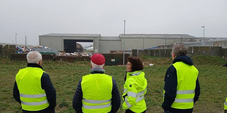 Personen tragen leuchtende Warnkleidung und Blicken im Rahmen einer Führung auf ein Entsorgungszentrum