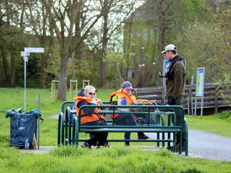 Drei Kinder sitzen auf einer Bank und verpflegen sich, daneben steht ein Naturparkmitarbeiter.