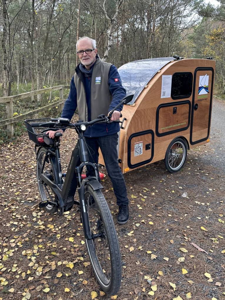 Mann mit einem Gespann aus E-Bike und Fahrrad-Wohn-Anhänger