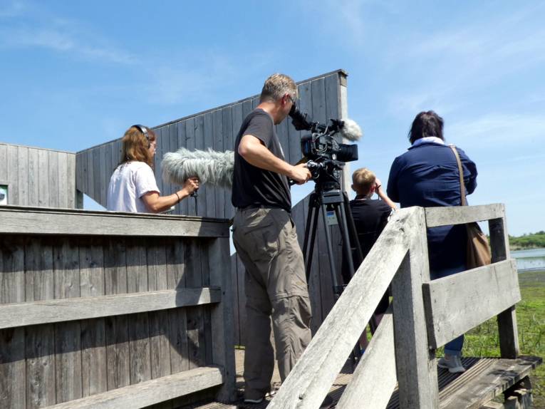 Eine Frau und ein Junge stehen auf einer Aussichtsplattform und schauen auf den Meerbruch im Naturpark Steinhuder Meer. Dahinter steht ein Filmteam und fängt die Szene in Bild und Ton ein.