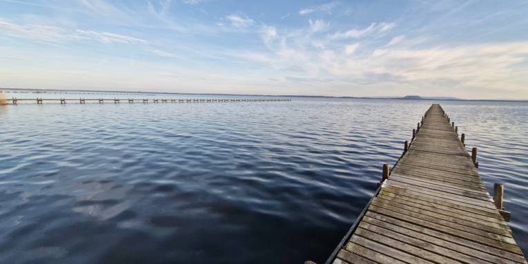 Blick über einen Steg und über das Steinhuder Meer bis zum gegenüberliegenden Ufer und den dortigen Kaliberg.