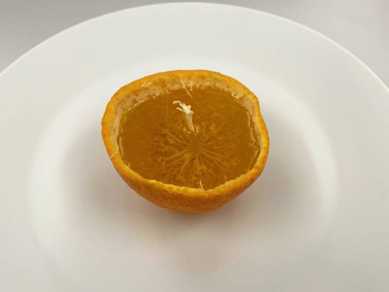 In der Schale einer halben Mandarine ersetzt Öl das Fruchtfleisch, der Strunk ragt in der Mitte über den Pegel des Öls hinaus.