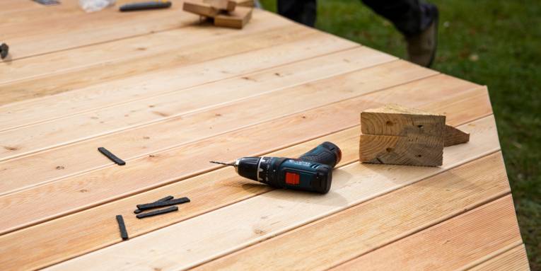 Ein Akkuschrauber liegt auf einem Holztisch, dazu Werkstücke aus Holz.