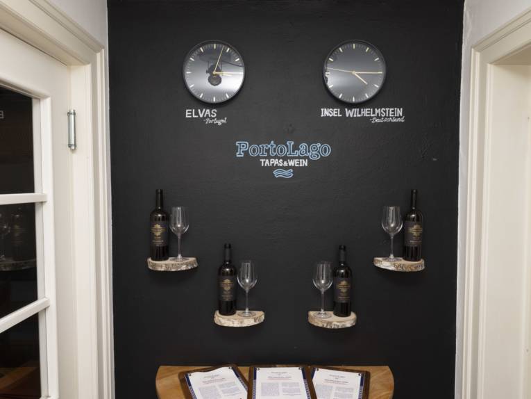 Dunkle Wand, zwei Uhren, die die Uhrzeit in Portugal und Deutschland anzeigen, Weine und Menükarte