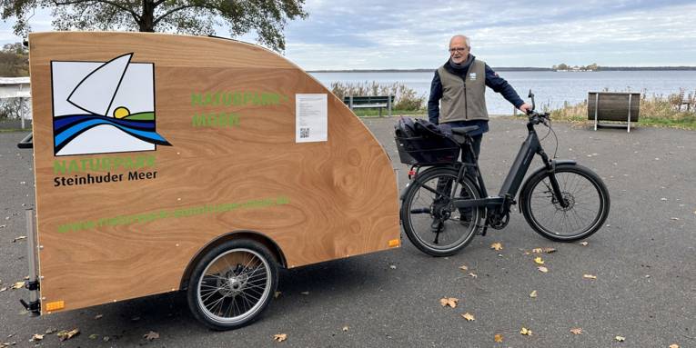 Mann mit einem Gespann aus E-Bike und Fahrrad-Wohn-Anhänger