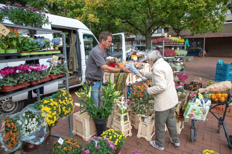 Eine Rentnerin nimmt Blumen von einem Blumenhändler auf dem Wochenmarkt entgegen.
