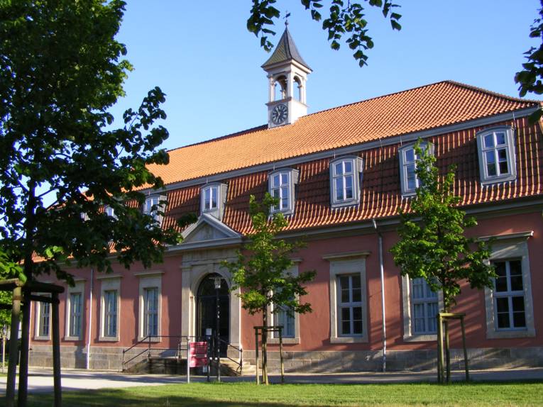 Blick auf ein großes, historisches Kurgebäude mit kleinem Uhr- und Glockentürmchenaufsatz auf dem roten Ziegeldach.