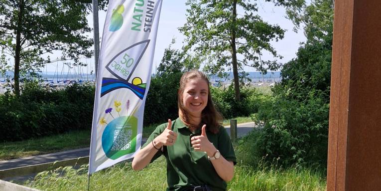 Porträtfoto einer Frau mit dem Steinhuder Meer im Hintergrund, sie reckt beide Daumen nach oben.