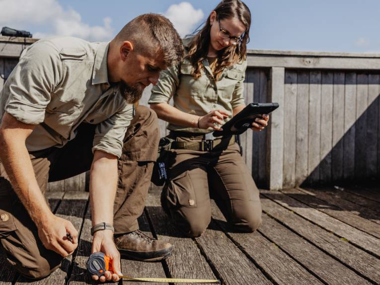 Eine Rangerin und ein Ranger knien auf einem Holzboden und messen etwas aus.