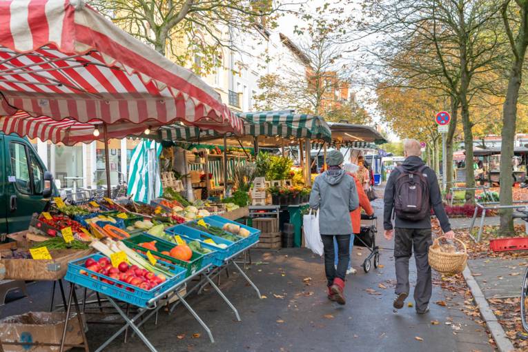 Kundschaft läuft zwischen den Wochenmarkt-Ständen.