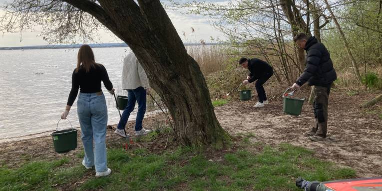 Vier Personen sammeln Abfall an einem Sandstrand.