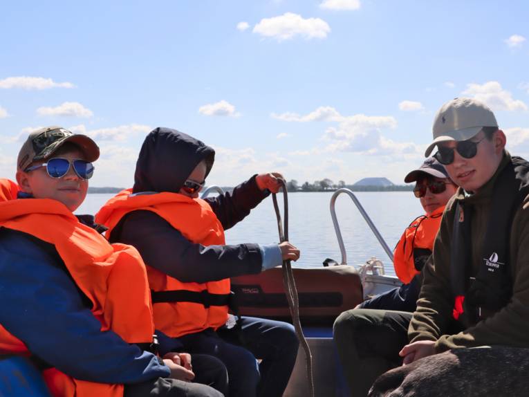 Drei Kinder sitzen mit einem Naturparkranger in einem Boot und üben Knoten.