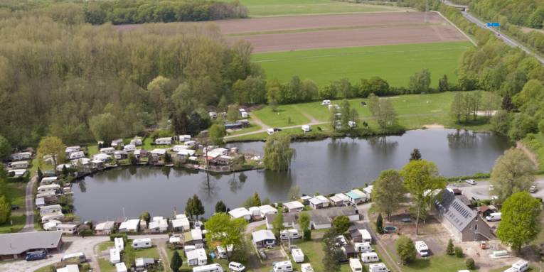 Luftaufnahme eines Natursees mit Gebäuden, Wohnwagen und Wald