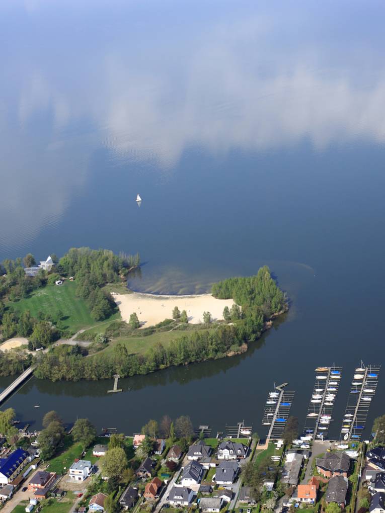 Blick aus einem Flugzeug auf das Ufer des Steinhuder Meeres mit Bootsanlegern und Wald und der Badeinsel.