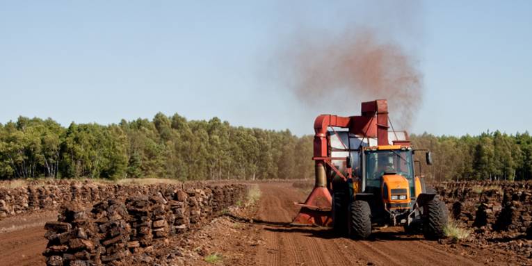 Torfballen im Moor und ein Trecker mit Spezialgerät für den Torfabbau
