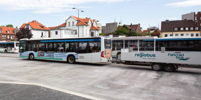 Hinter einem Linienbus hängt ein Anhänger.