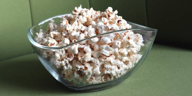 Popcorn in einer Glasschüssel auf einem grünen Sessel.