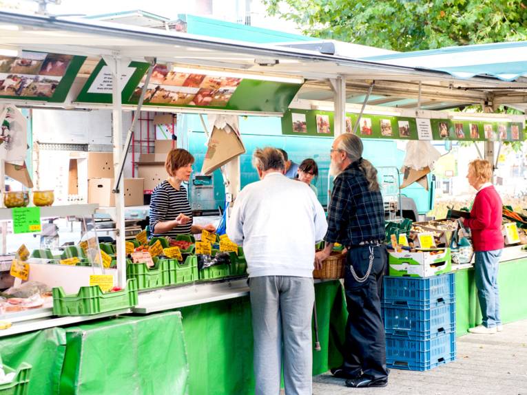 Kunden im Gespräch mit Gemüsehändlerinnen an einem Marktstand