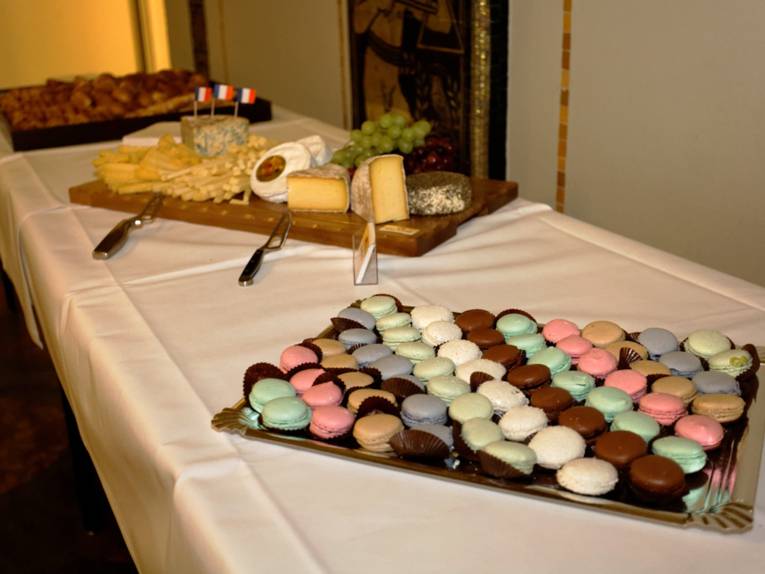 Ein Tablett mit Macarons im Vordergrund, ein Brett mit verschiedenen Käsesorten im Hintergrund