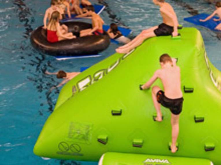 Kinder im Schwimmbad auf einem aufgeblasenen, grünen Berg und auf riesigen Schwimmreifen