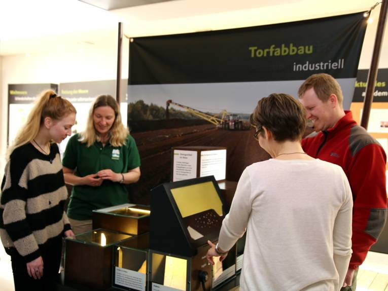 Drei Besucherinnen und ein Besucher entdecken die Themeninsel "Torabbau industriell".