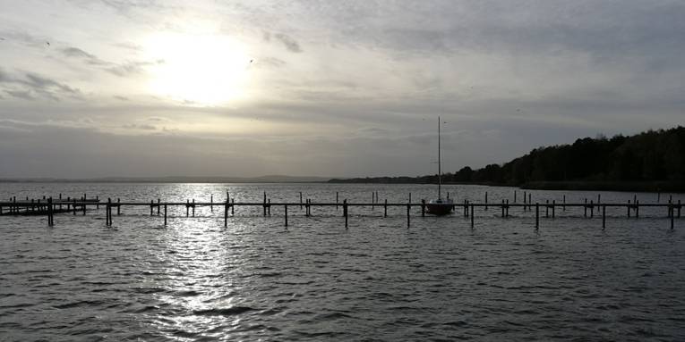 Über einem Steg am Steinhuder Meer geht die Sonne unter. An dem Steg ist ein einzelnes Boot vertäut.