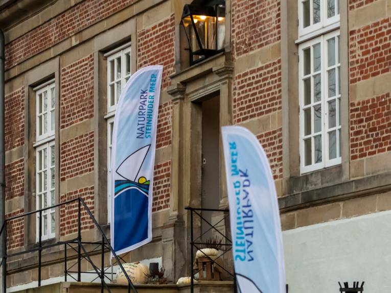 Zwei Beachflags mit dem Logo des Naturparks Steinhuder stehen auf einer Treppe zu einem Eingang von Schloss Landestrost in Neustadt am Rübenberge.