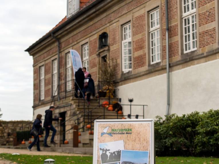 Menschen betreten Schloss Landestrost über eine Treppe, im Vordergrund informiert ein Display über die Steinhuder Meer Konferenz 2017.